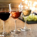 three glass of white red and rose wine with dim light in wooden restaurant table with a grape background